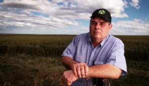 Terry Schmucker leaning on a fence in front of his wheat farm.