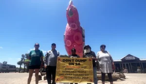 Members of Barngarla community holding a banner which reads "don't dump on SA." They are standing in front of a large sculpture of a pink galah