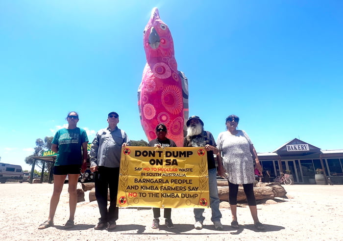 Members of Barngarla community holding a banner which reads "don't dump on SA." They are standing in front of a large sculpture of a pink galah